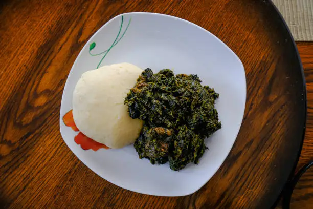 Traditional African meal with greens and ugali Plate of white ugali served with dark leafy vegetable stew on a wooden table