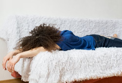 Relaxing at-home rest on cozy sofa Person lying face down on a white furry couch, arms hanging over the edge