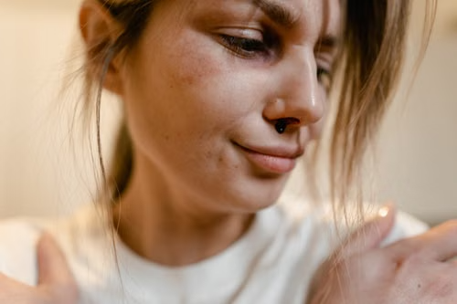 Contemporary portrait showcasing septum piercing style Close-up of a person with a nose piercing looking down and touching their face